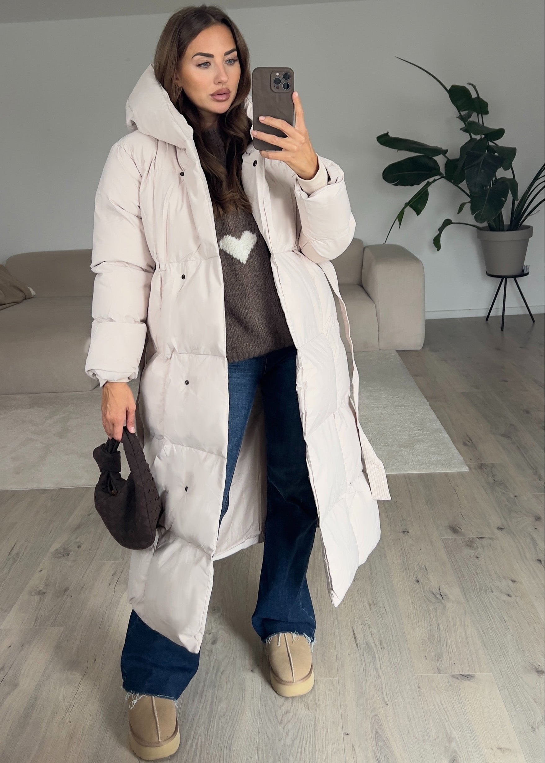 Modell trägt einen langen Damen Steppmantel mit Kapuze und Taillengürtel – NAHA Wintermode