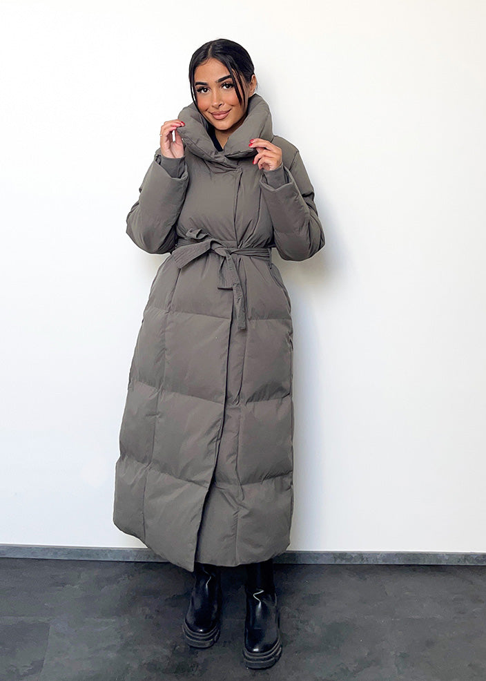 Frau trägt lange graue Winterjacke mit Gürtel & Stehkragen – moderner Winterlook von NAHA