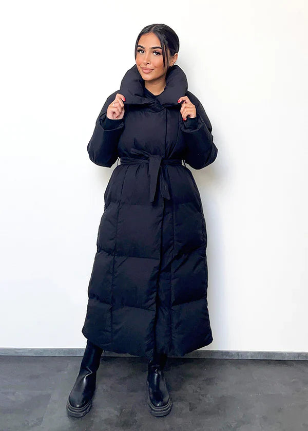 Frau trägt lange Winterjacke in Schwarz mit Gürtel & hohem Kragen – eleganter Winterlook von NAHA