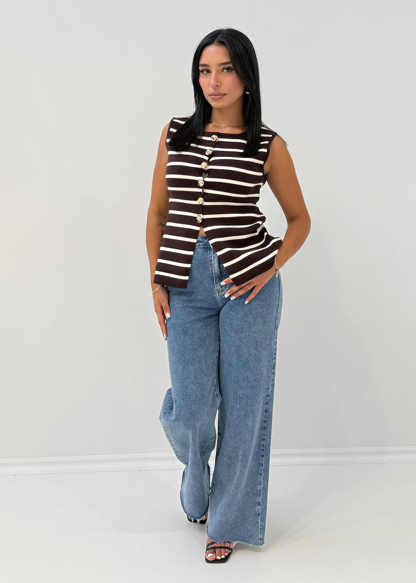 Modell trägt ärmellose, gestreifte Strickweste mit goldenen Knöpfen und Rundhalsausschnitt zu Jeans