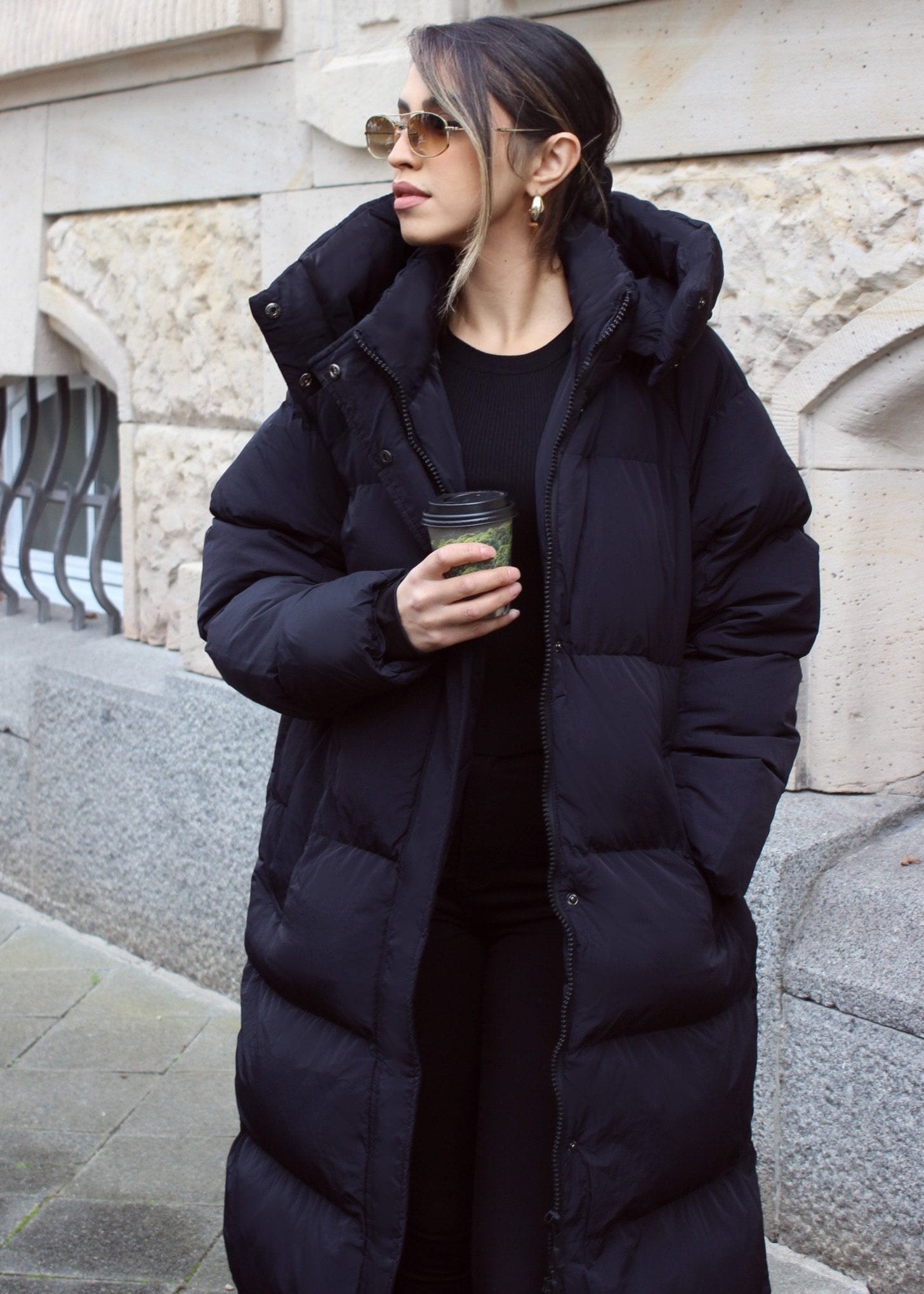 Modell trägt lange schwarze NAHA Steppjacke mit Kapuze – perfekter Winterlook für kalte Tage.