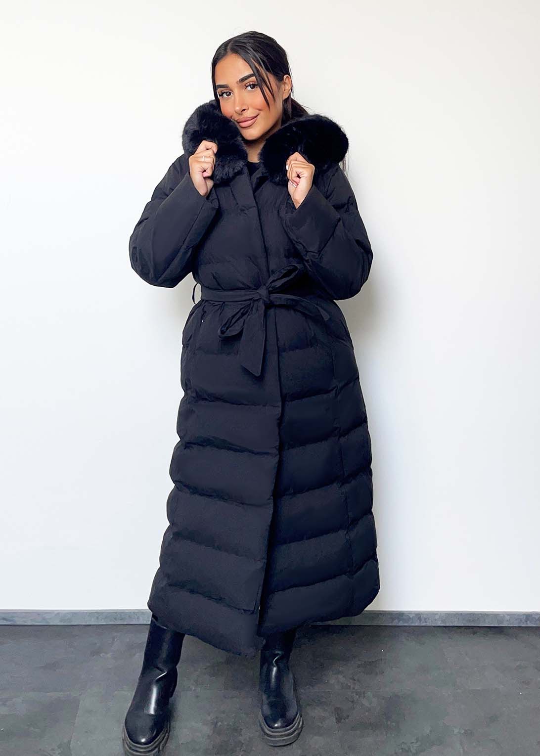 Modell trägt einen langen Damen Steppmantel mit Kapuze und Taillengürtel – NAHA Wintermode