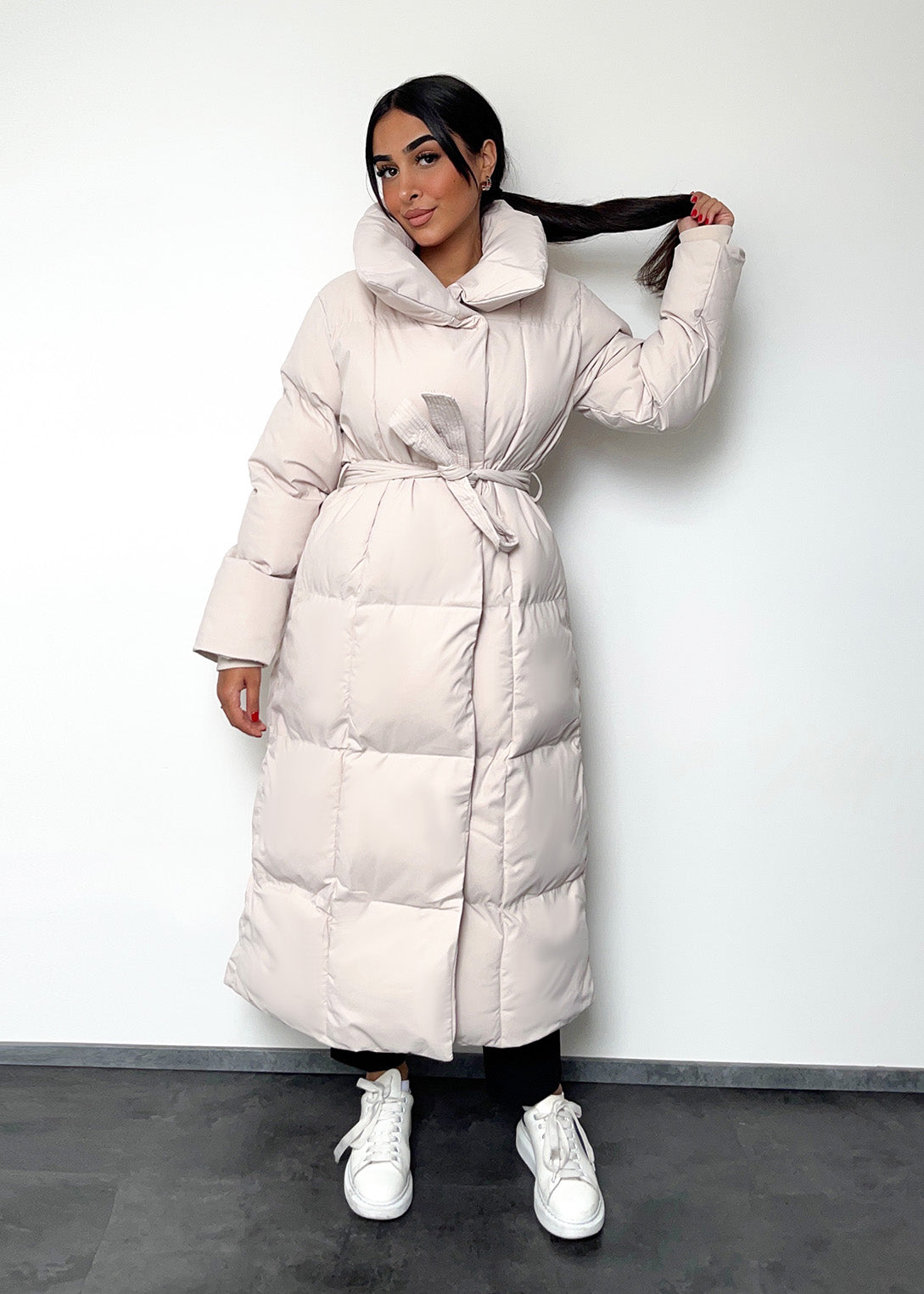 Frau trägt lange Winterjacke in Beige mit Gürtel & Stehkragen – eleganter Winterlook von NAHA