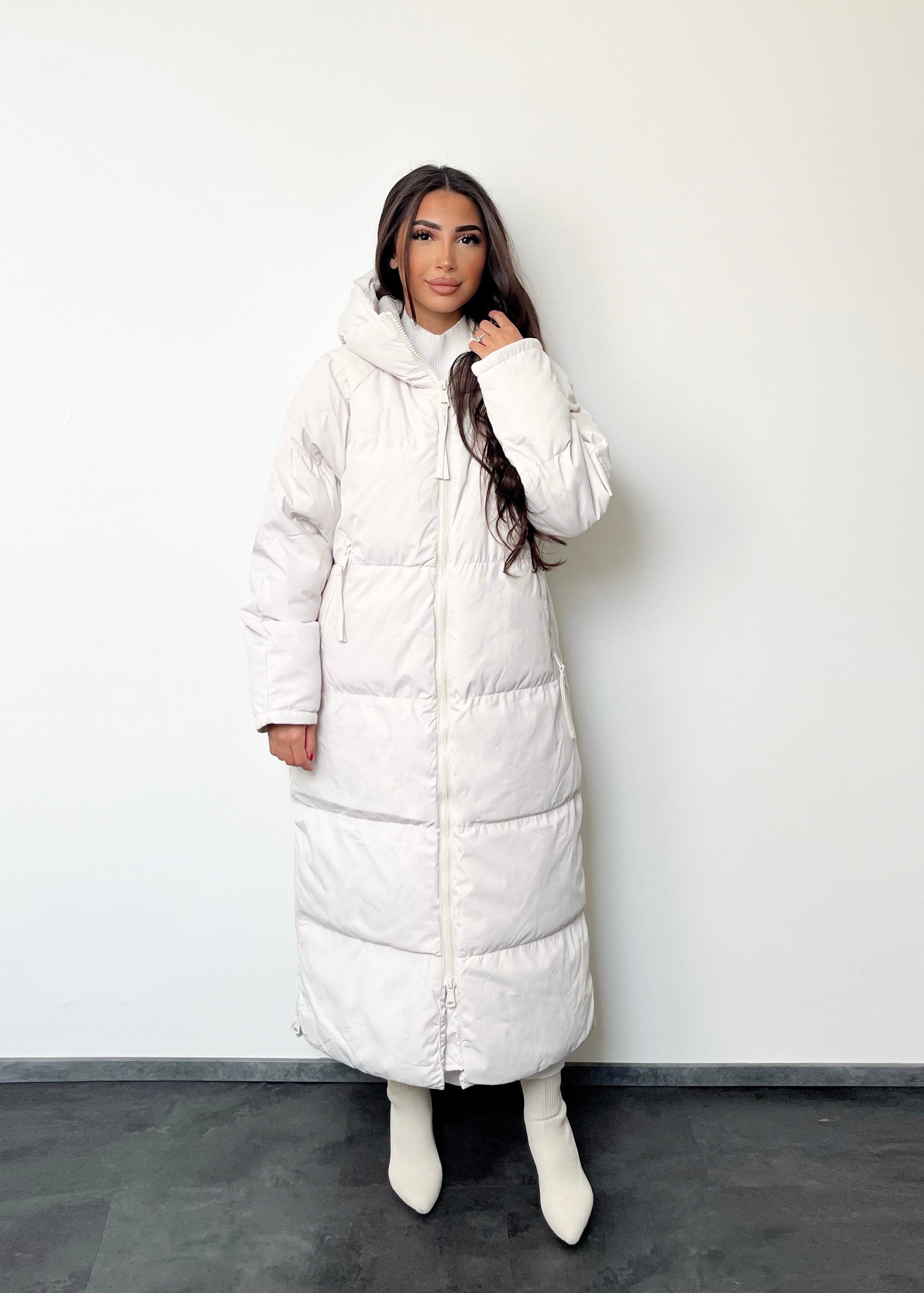Modell trägt einen langen Damen Steppmantel mit Kapuze und durchgehendem Reißverschluss – NAHA Fashion