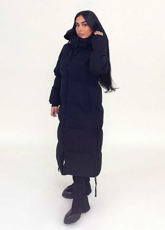 Modell trägt einen langen Damen Steppmantel mit Kapuze und seitlichen Reißverschlüssen – NAHA Wintermode