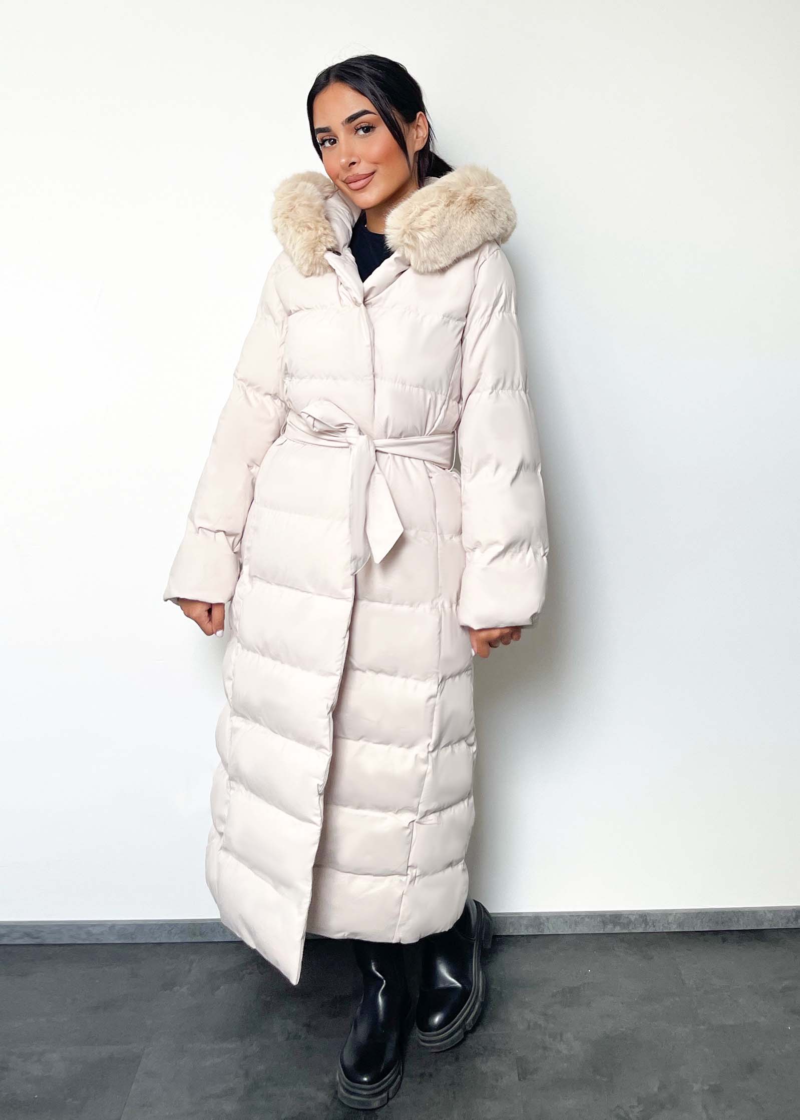 Modell trägt einen langen Damen Steppmantel mit Kapuze und Taillengürtel – NAHA Wintermode  